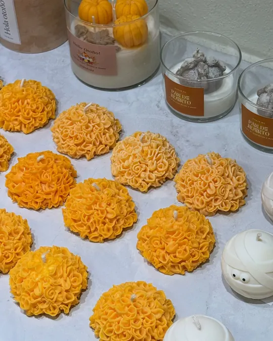 Velas en forma de flor de cempasúchil, naranjas, sobre una mesa blanca