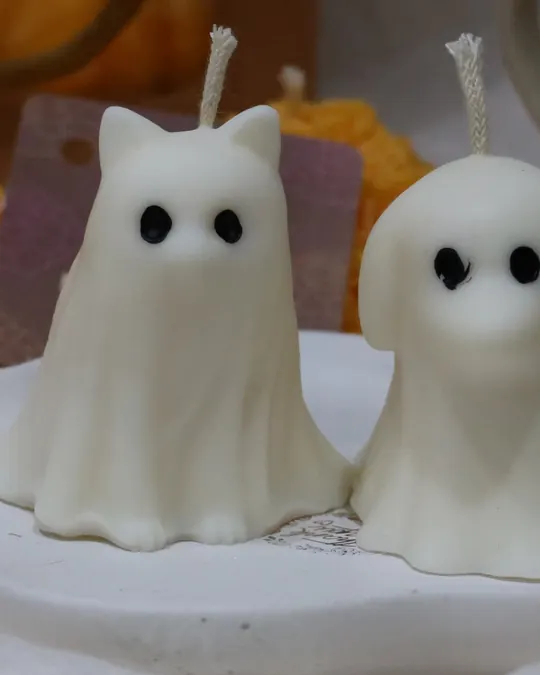 Dos velas blancas en forma de fantasma, una con orejas de gato y otra de perrito