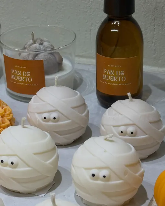 Velas blancas en forma de momia con ojos, junto a la vela y el aromatizante Pan de muerto